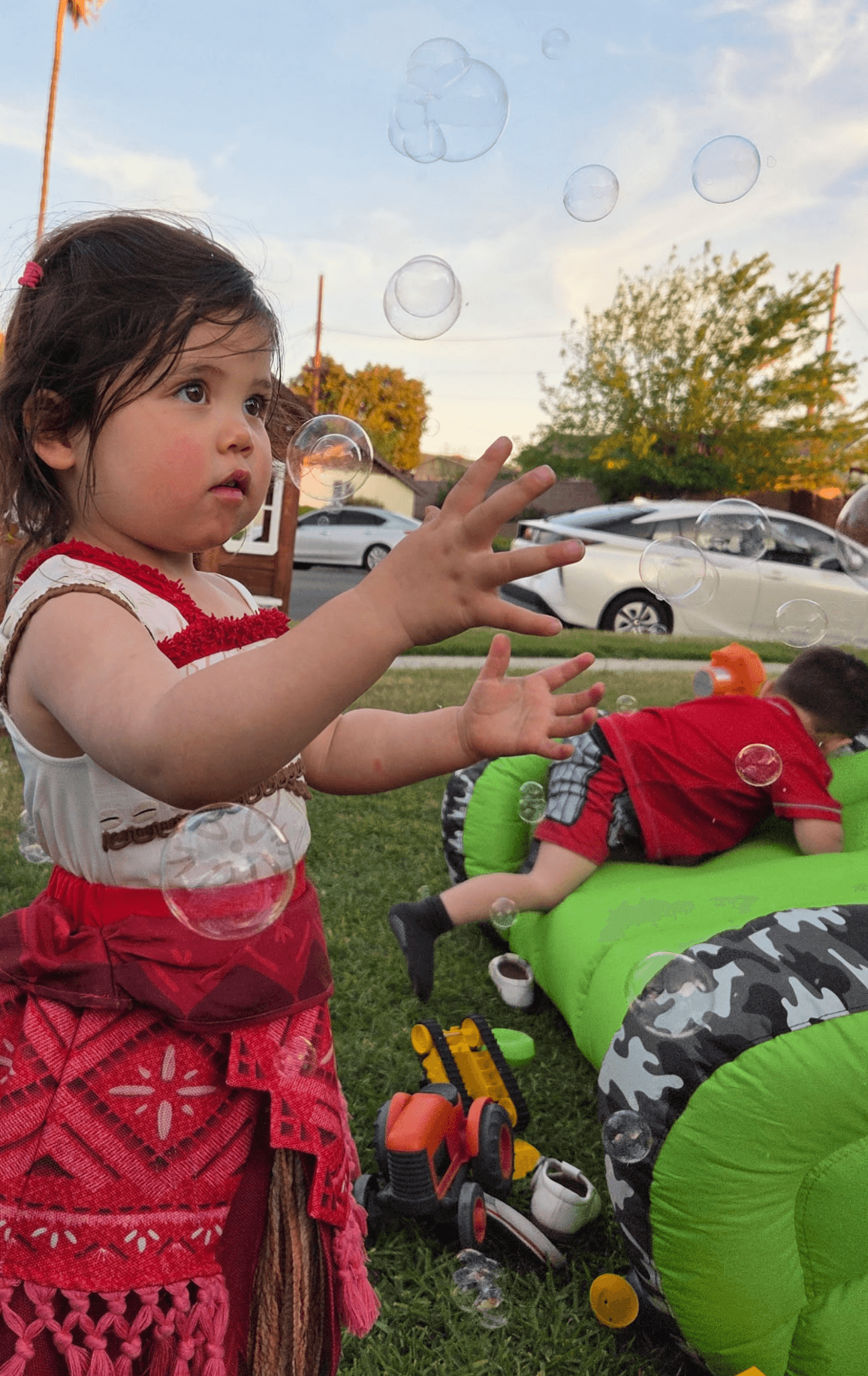 Child reaching for bubbles in a sunny backyard